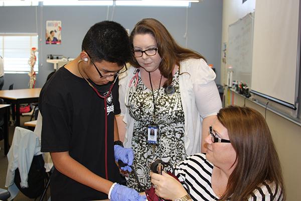 While taking dean Sherrae Nelsons blood pressure, Sophomore John Paul Avenido is aided by Mrs. Donna Hatch to ensure an accurate reading.