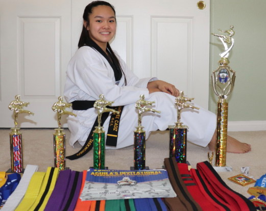 Displaying all of the awards she has earned through the years, sophomore Marivee Cadiz poses with her black belt. “It gives me a sense of life and purpose when I step on the taekwondo mat,” Cadiz said. “It gives me a reason to keep going and learn from my mistakes and improve them. Even though the sport isn’t easy, it gave me a reason to work harder, but also smarter. It gives me lessons that I could use in reality, not only self-defense, but also improves my mental health.”
