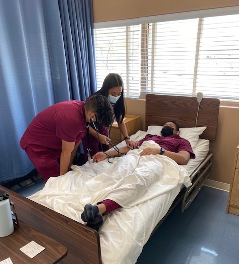 Rehearsing the skills needed to do clinicals, senior Shinikee Garcia and Vincent Garcia check senior Michael Ennis’ pulse. Students began clinicals on Friday and will be learning the perks of being a CNA. “At first, I was nervous to go to clinicals because it’s very different interacting with a mannequin or a classmate you’ve known for a while compared to actual patients,” Garcia said. “However, when I got to the facility everyone was welcoming and the residents were really nice. The residents are all veterans who have been through a lot so it’s comforting to see a smile on their face while helping with daily activities like changing their bed.”  Photo Credit: Cassandra Trummel
