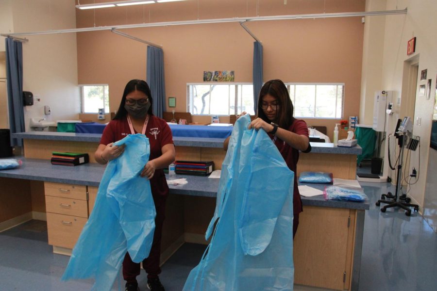 As students adjust to the sudden change, senior Trinity Mendeguarin and junior Valeria Gonzalez practice donning and doffing personal protective equipment. Changes have been made to the skills that are taught and tested, condensing many of them into smaller steps. “Students may not be prepared to work in the clinical site,” Nursing teacher Cassandra Trummel said. “I think that they’ll be fine and prepared to take the test, but I think that it will be overwhelming for them when they get a job in that field and at clinicals since it will look a lot different than what is done in the classroom.”
