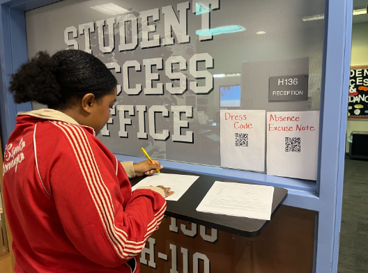 Standing in front of the student success office, senior Daphney Garcia-Hatton fills out the student portion of the newly enforced absence excuse note. Students are required to turn in physical excuse notes signed by their parent or guardian. “A lot of people find it inconvenient that the excuse notes are now physical, but it prevents students from filling it out on their own at home online,” Garcia-Hatton said. 