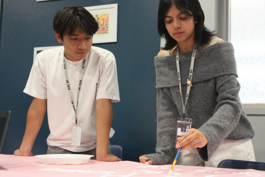 Completing a poster, sophomores Alejandro Merino and Yara Ahmed are preparing to promote today's event.  They had finished decorations for the event after weeks of work. “Yara and I worked hard to finish this poster before we had to hang it up,” Merino said. “We all have to make designs and then get them approved by our supervisors before executing them. I did the sketching and she did the painting so we could collaborate effectively”.