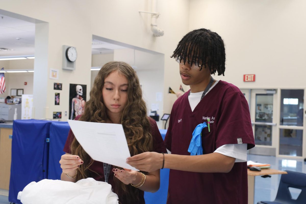 Examining a sheet of tasks, junior Bryan Pratt assists a classmate with reviewing for the practical skills test. Senior students in the Nursing program are required to take the Pharmacy course, where they would then be eligible choose if they wanted to go on the trip to the exhibition. “I’m excited to go on that trip next year,” Pratt said. “I want to be a doctor and I like the human body so it would be nice for a guide to explain it more in detail.”